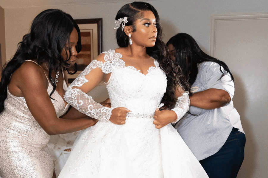 A woman in a wedding dress is being fitted by two women.